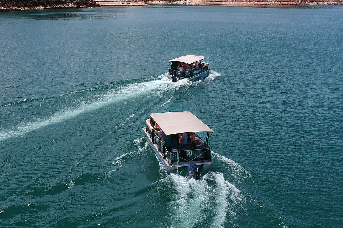 Dois barcos modelo Pontoon navegando nas águas calmas de um lago em um dia ensolarado, representando liberdade e turismo náutico.