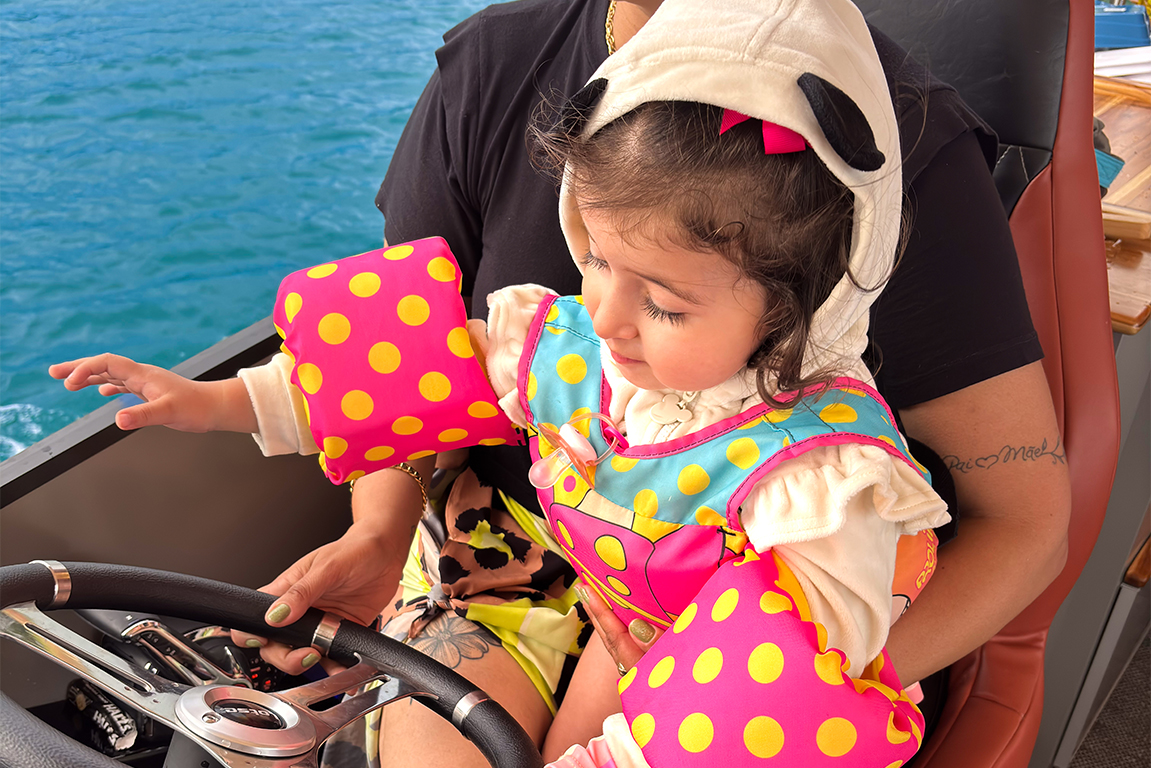 Criança segurando o volante da embarcação com supervisão de um adulto, ilustrando a segurança e os momentos em família proporcionados pelo Pontoon.