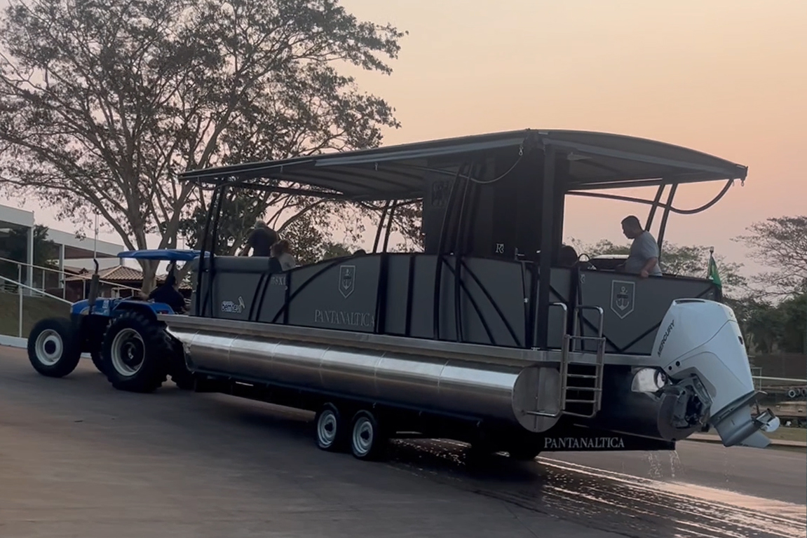 Pontoon Boat sobre carreta de reboque sendo transportado em pátio de marina